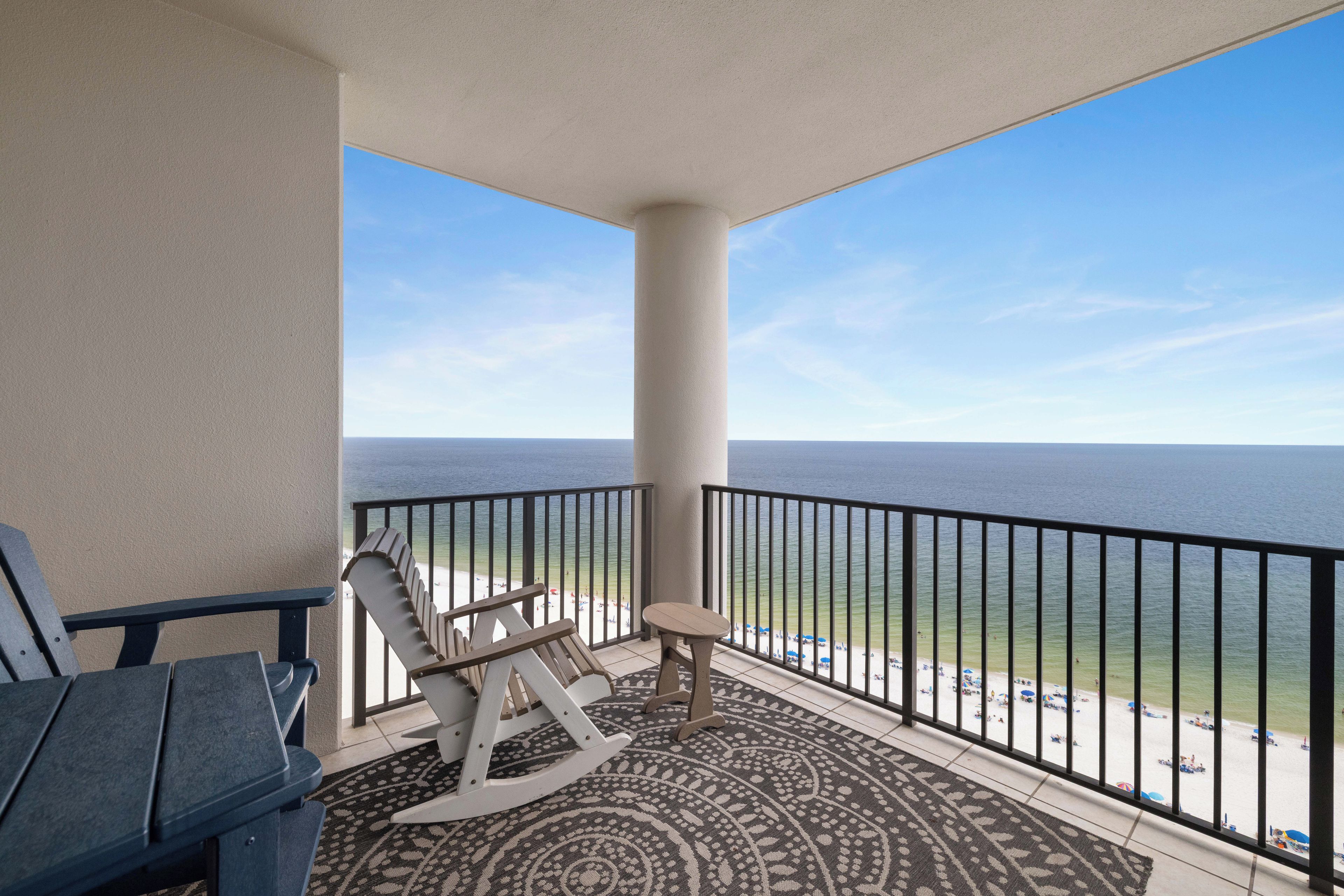 A balcony with a view of the ocean, a rocking chair, and a table.