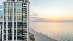 A high-rise building with multiple balconies overlooking a beach at sunset.