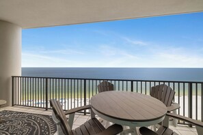 A balcony with a view of the ocean, a round table, and four chairs.