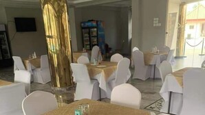 Une salle de banquet avec des tables rondes recouvertes de nappes blanches et des chaises, une grande colonne dorée et un distributeur automatique en arrière-plan.