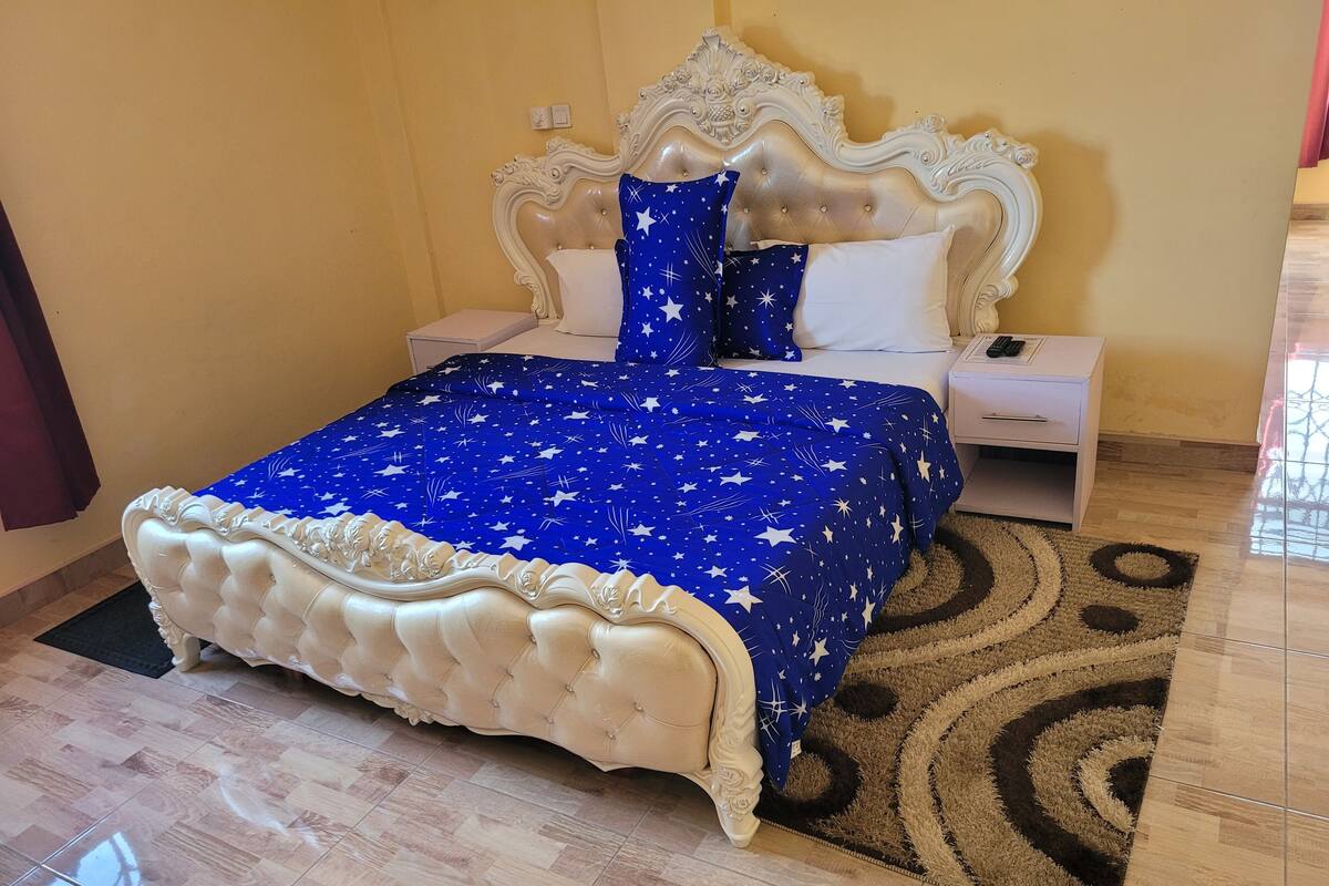 Un dormitorio con una cama grande, una mesita de noche, un aparador blanco y una alfombra estampada.
