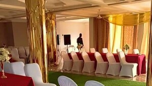 Une salle de banquet avec des rangées de chaises blanches, des nappes rouges et des éléments décoratifs dorés.