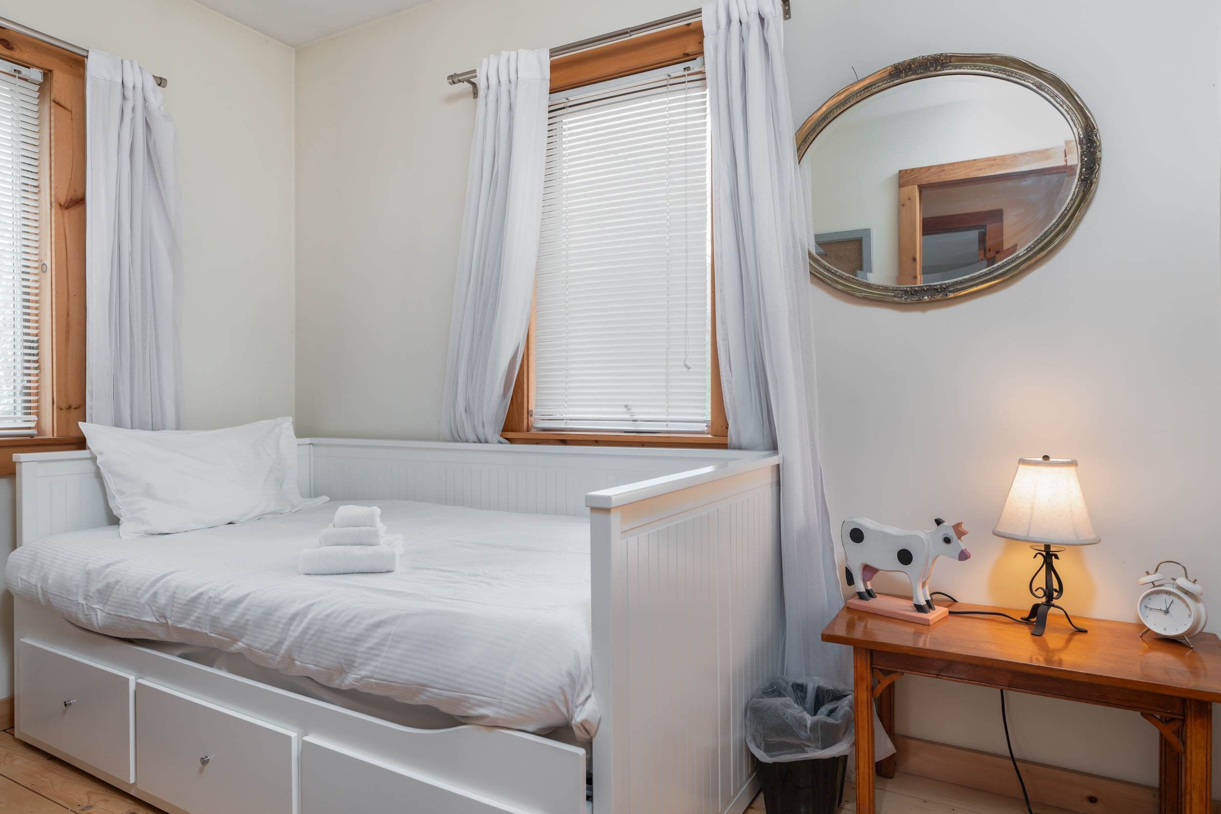 Une chambre à coucher avec un lit, une table de chevet avec une lampe, un miroir et une fenêtre avec des rideaux.