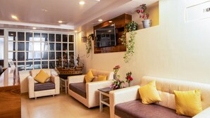 A modern living room with a wooden ship model, two sofas with yellow cushions, and a TV mounted on the wall. - Hotel Raj Ville (Darjeeling)