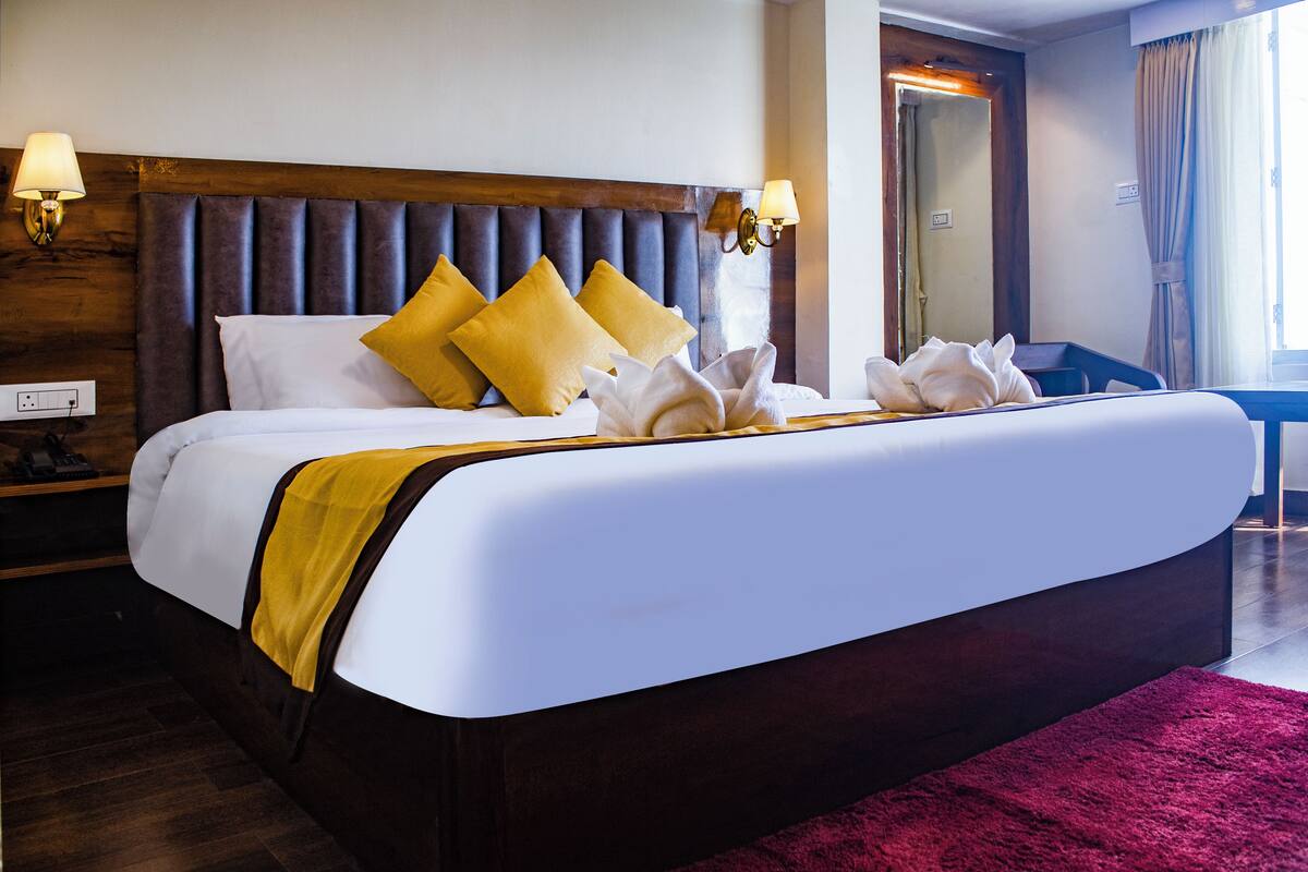A neatly made bed with white and yellow bedding, a wooden headboard, and a red rug.