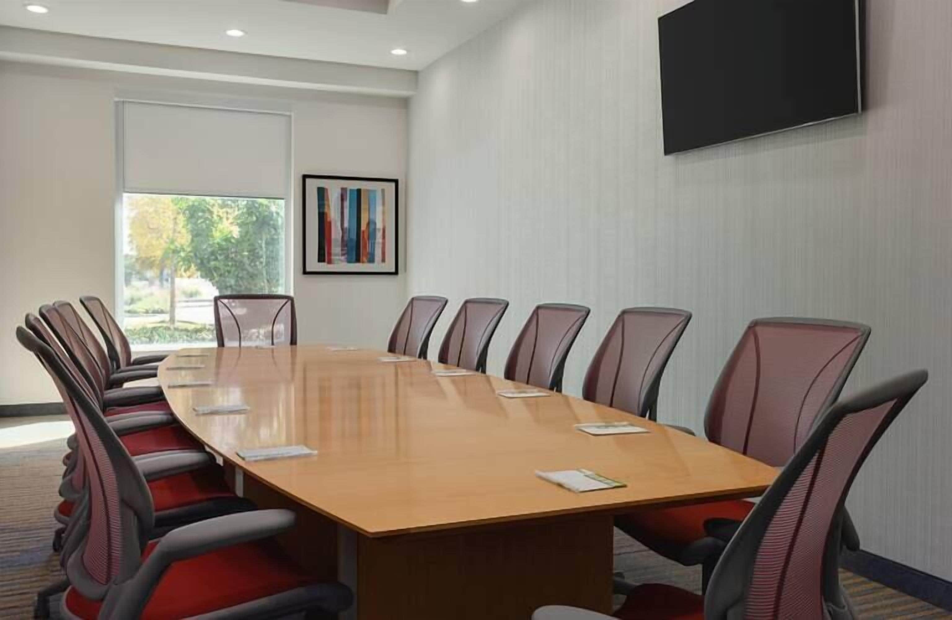 A conference room with a long table and 10 chairs, a large window, and a mounted TV.