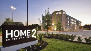 A hotel sign for Home 2 Suites by Hilton, featuring a modern building with a stone facade and a well-maintained lawn area. - Home2 Suites By Hilton Austin South I-35 (Austin)