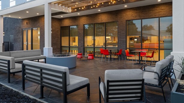 An outdoor seating area with modern furniture, a fire pit, and a covered patio with string lights. - Home2 Suites By Hilton Austin South I-35 (Austin)