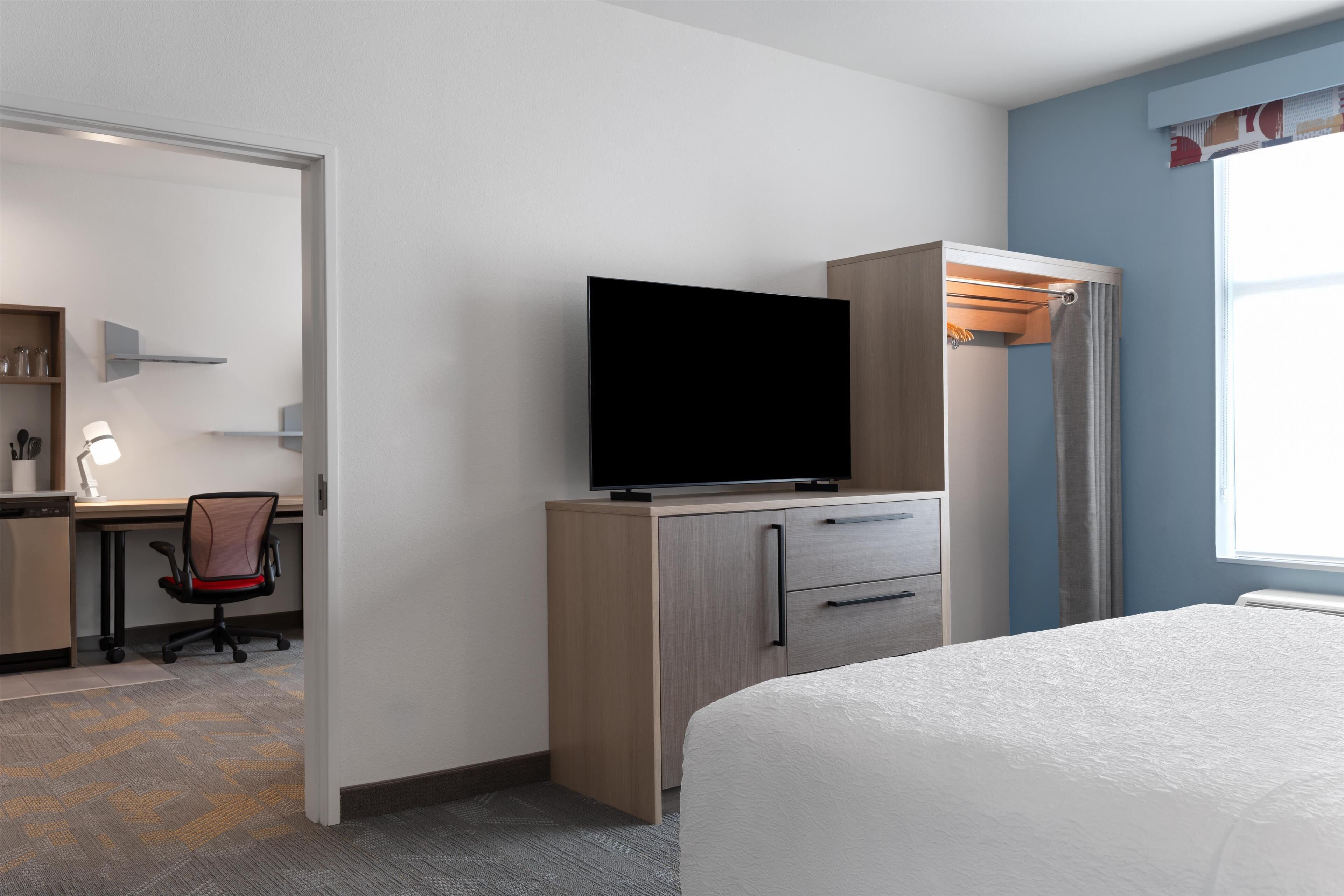 A hotel room with a bed, a desk with a chair, a television, and a wardrobe.