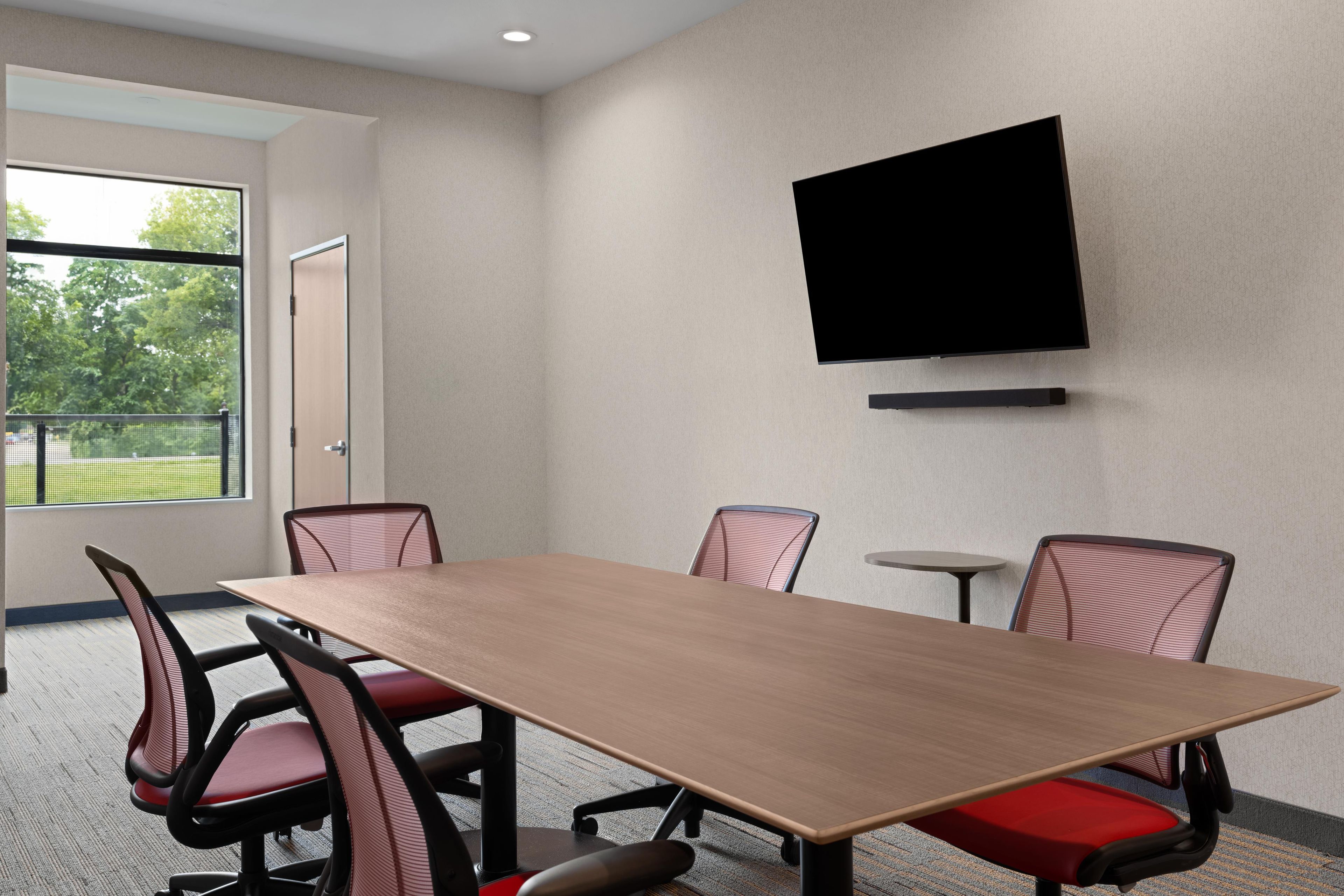 A conference room with a long table, four chairs, a small round table, and a mounted TV.