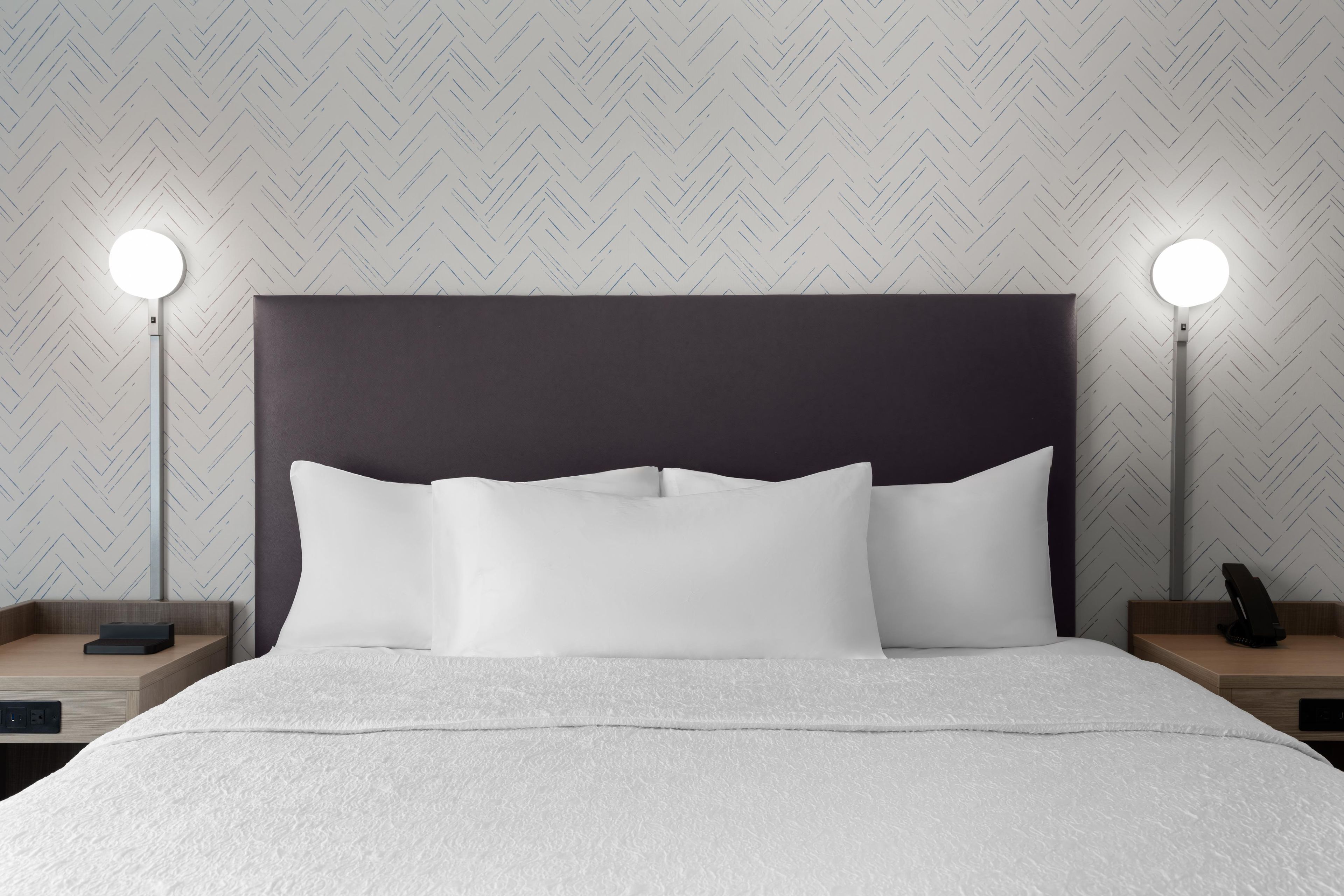 Una cama bien tendida con ropa blanca y un cabecero oscuro, flanqueada por dos mesitas de noche con lámparas.