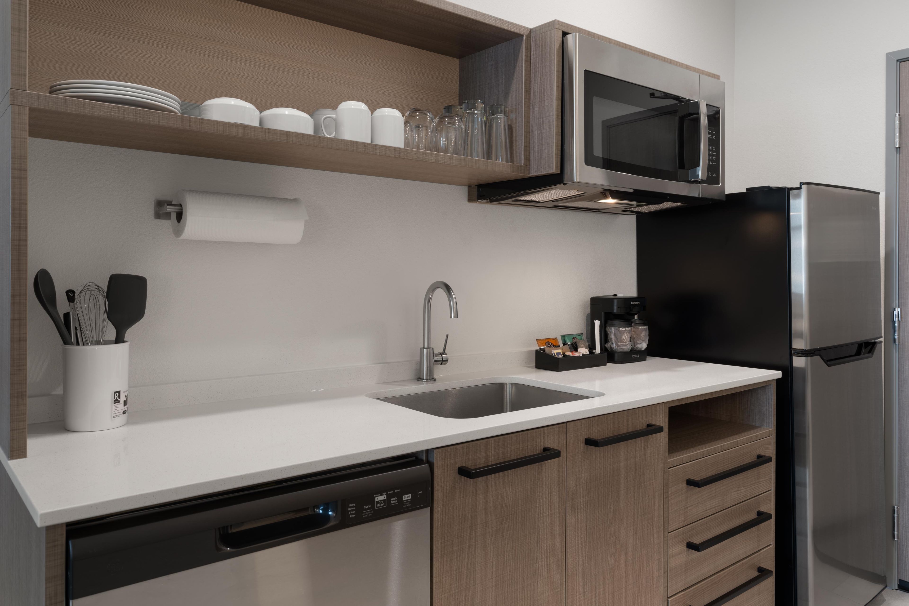 A modern kitchen with a stainless steel refrigerator, a microwave, a dishwasher, and wooden cabinets.