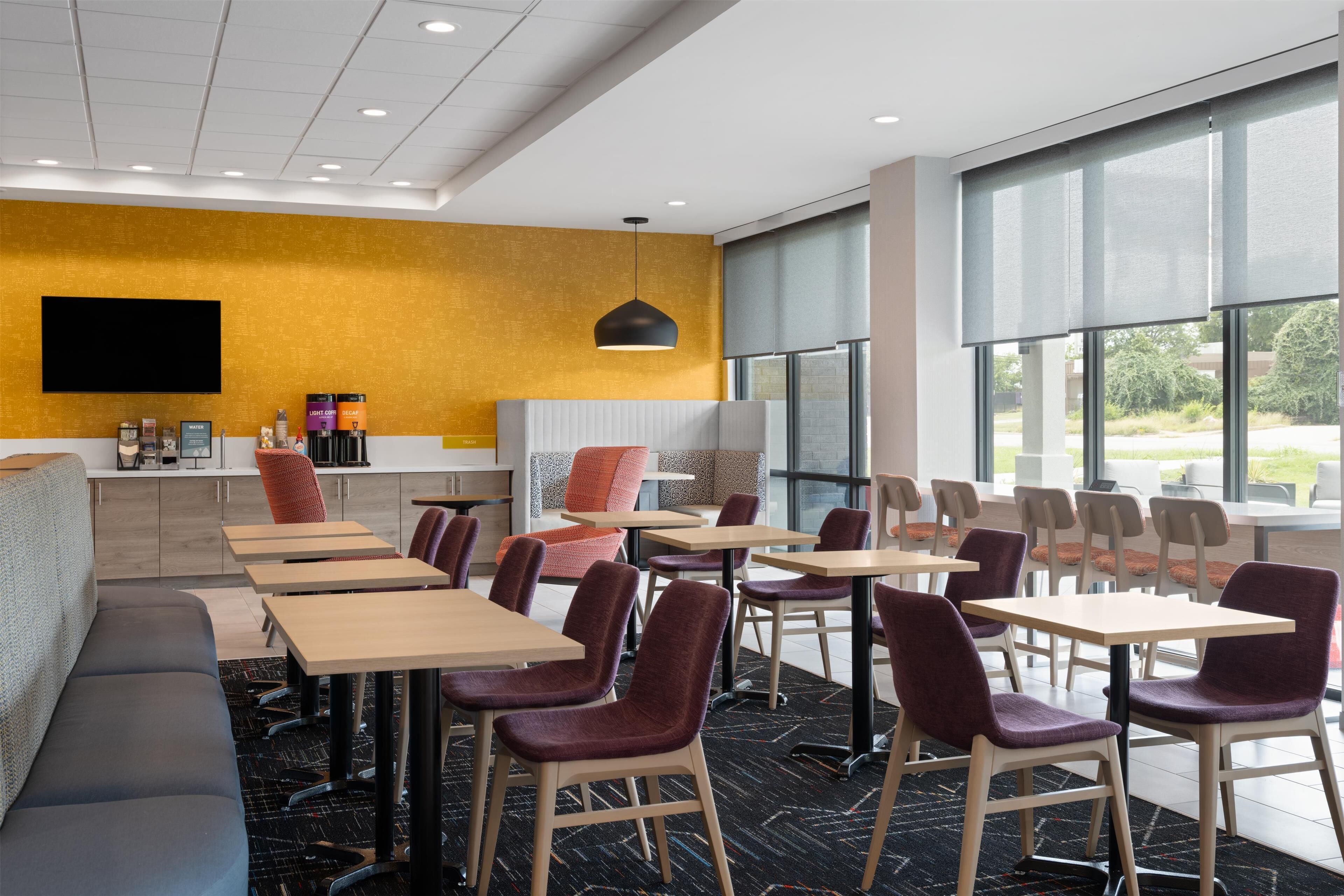 Un hall d’hôtel moderne, doté d’un espace salon, de tables et d’une grande fenêtre offrant une vue sur l’extérieur.