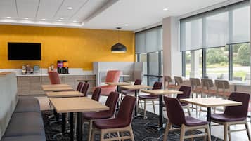 Un hall d’hôtel moderne, doté d’un espace salon, de tables et d’une grande fenêtre offrant une vue sur l’extérieur.