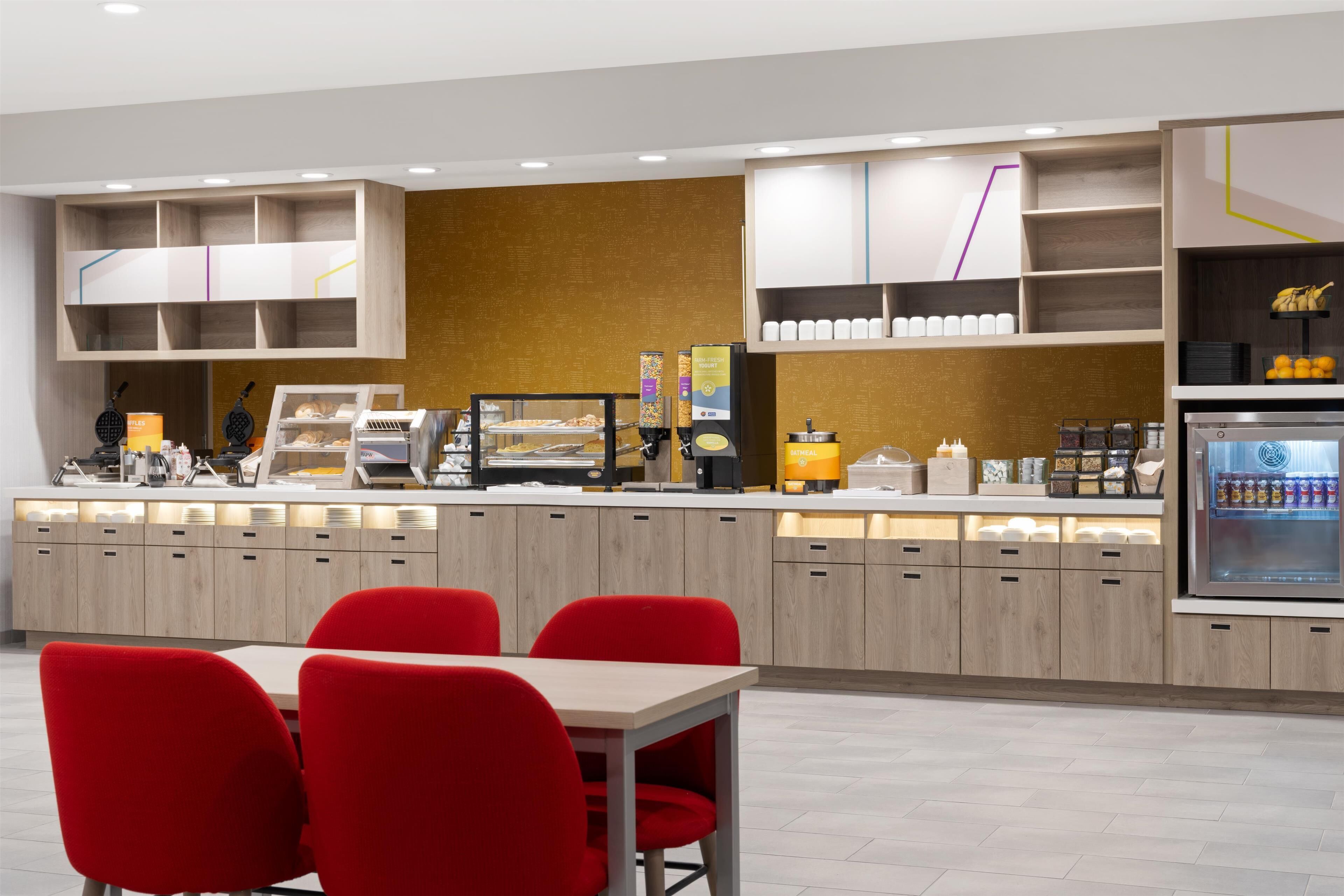 A modern cafe with a wooden counter, red chairs, and a refrigerator stocked with beverages.