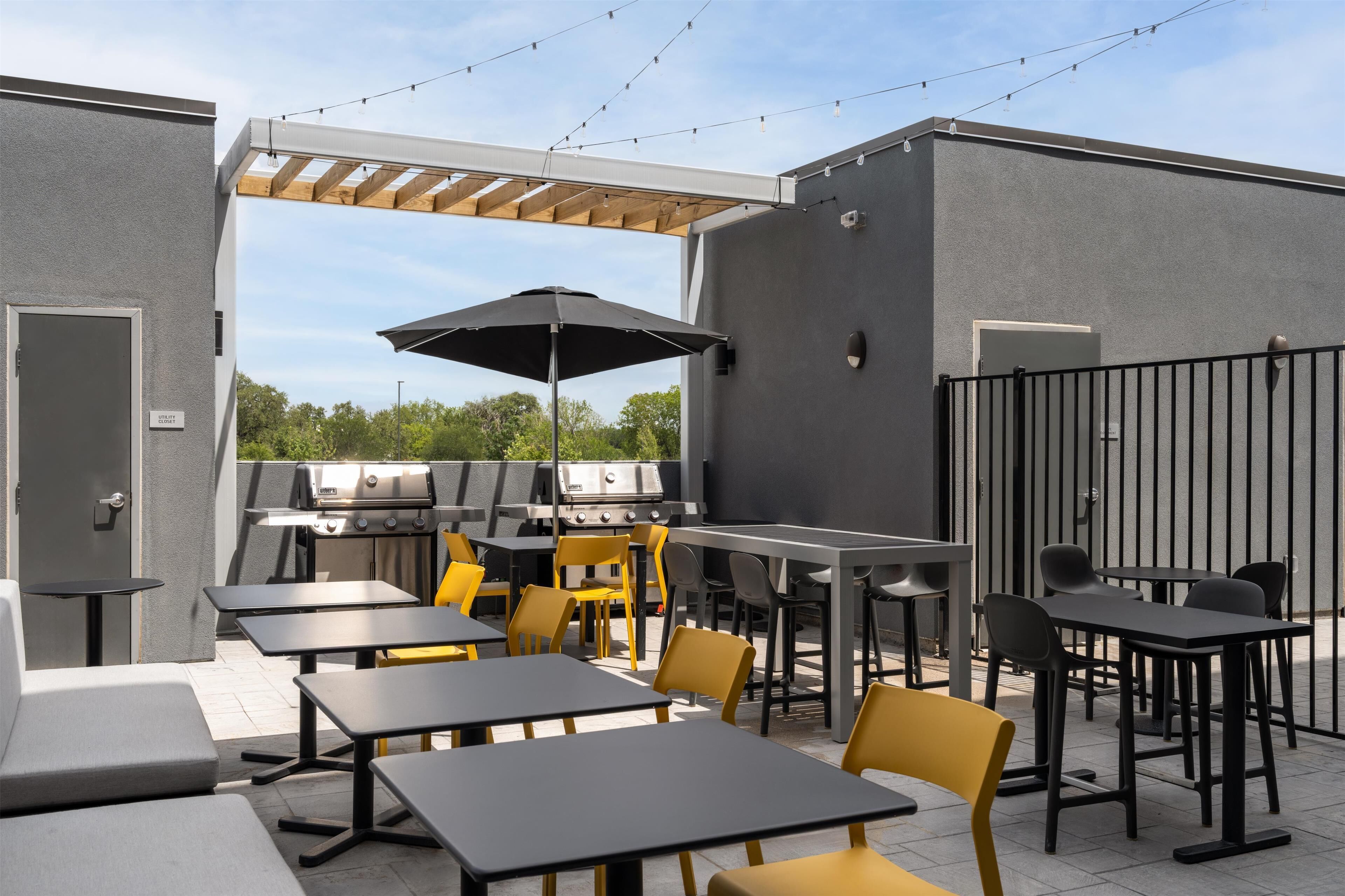 An outdoor patio with tables and chairs, a grill, and a pergola.