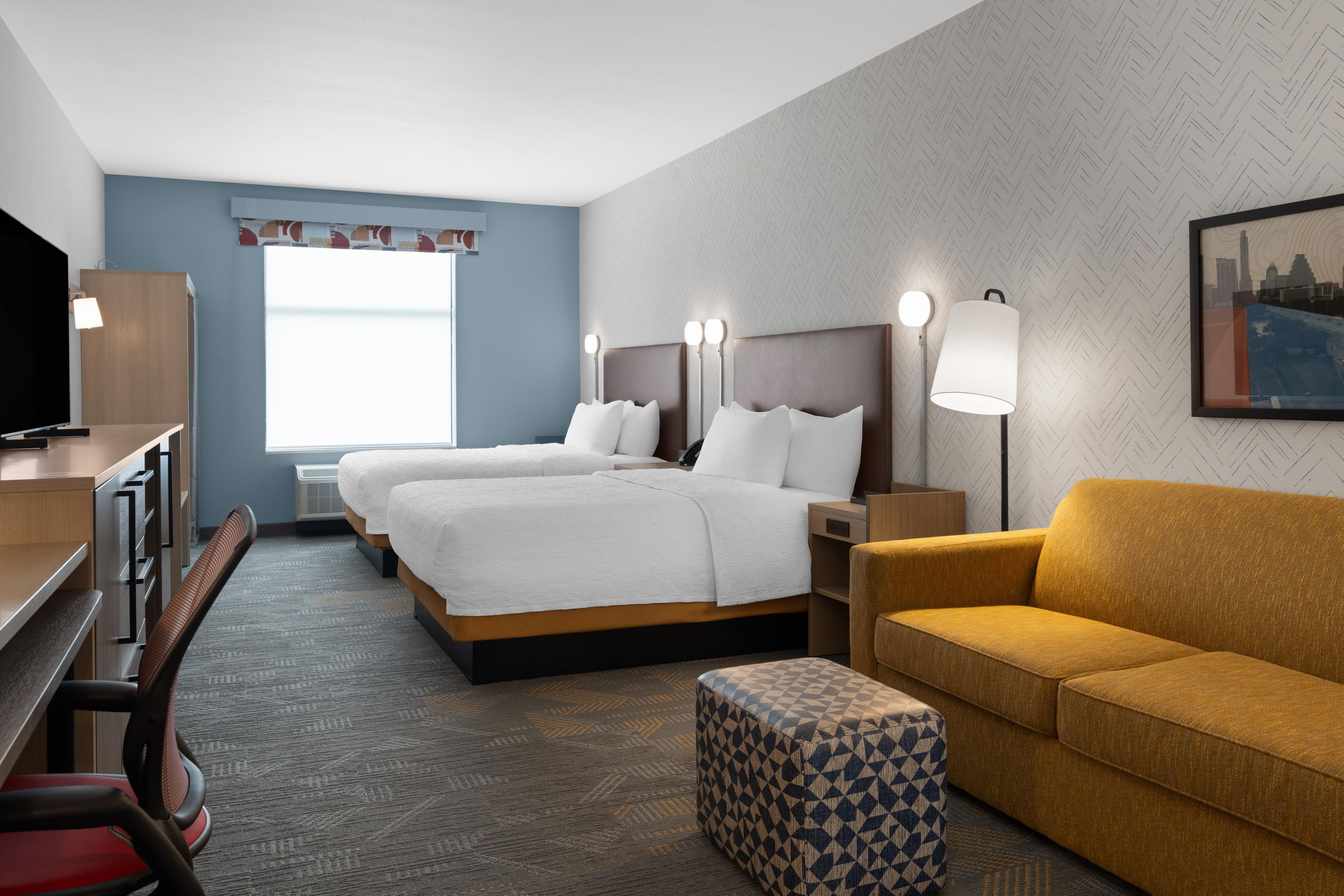A hotel room with two beds, a sofa, a TV, and a cityscape painting.