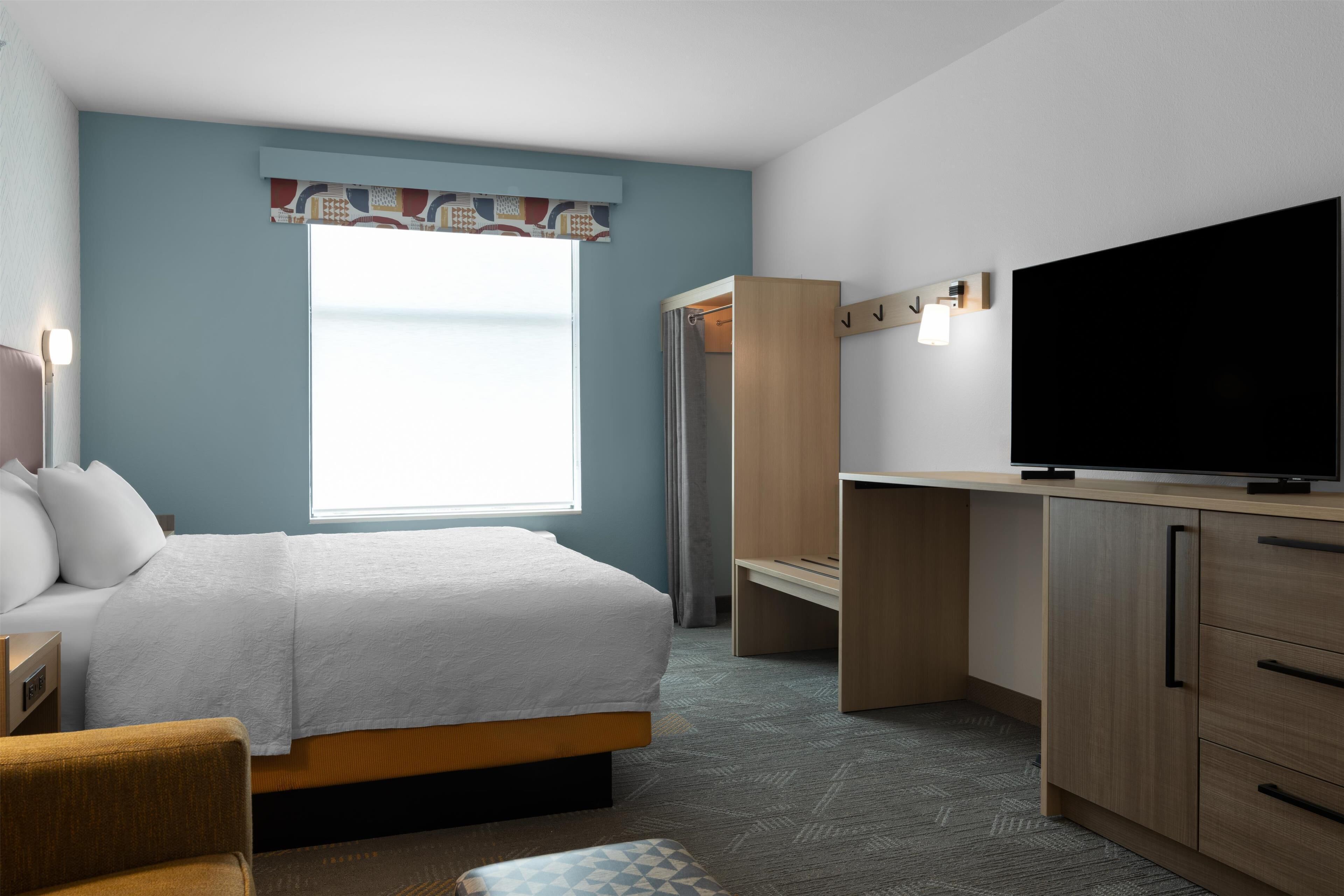 A hotel room with a bed, a desk, a television, and a wardrobe.