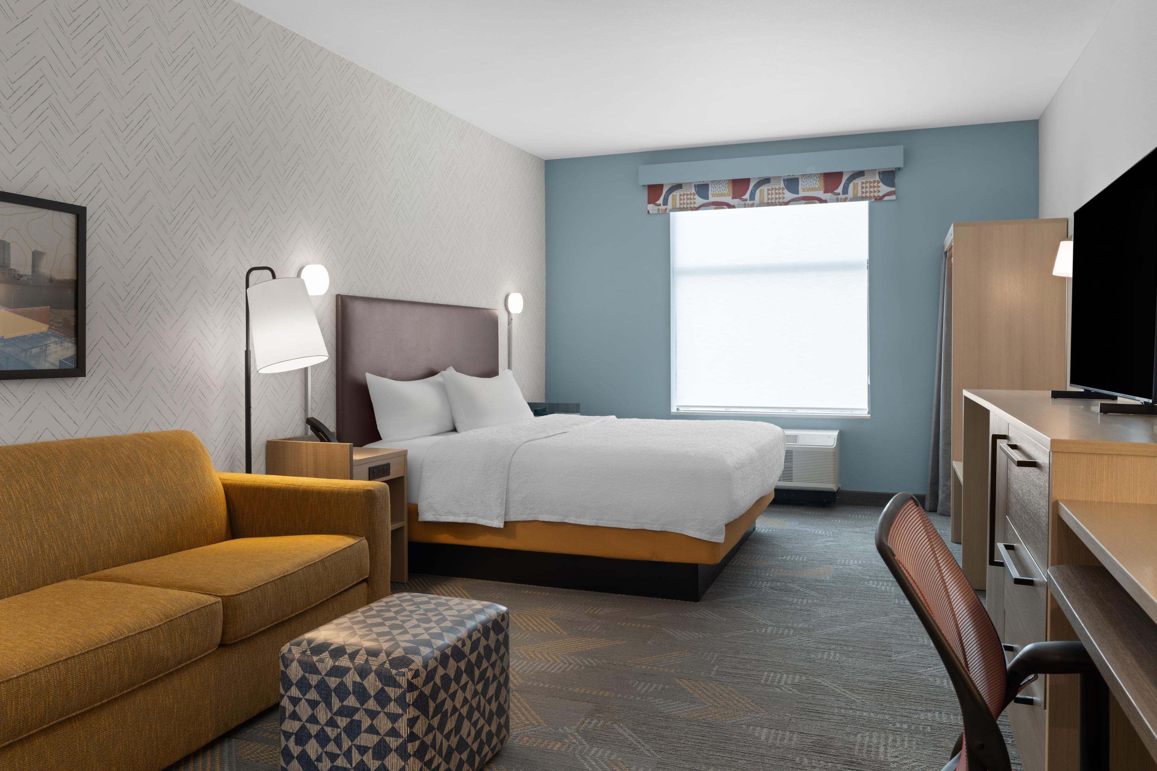 A hotel room with a bed, a sofa, a desk, a television, and a window.