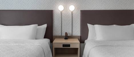A hotel room with two beds, a nightstand with a lamp, and a herringbone-patterned wall.