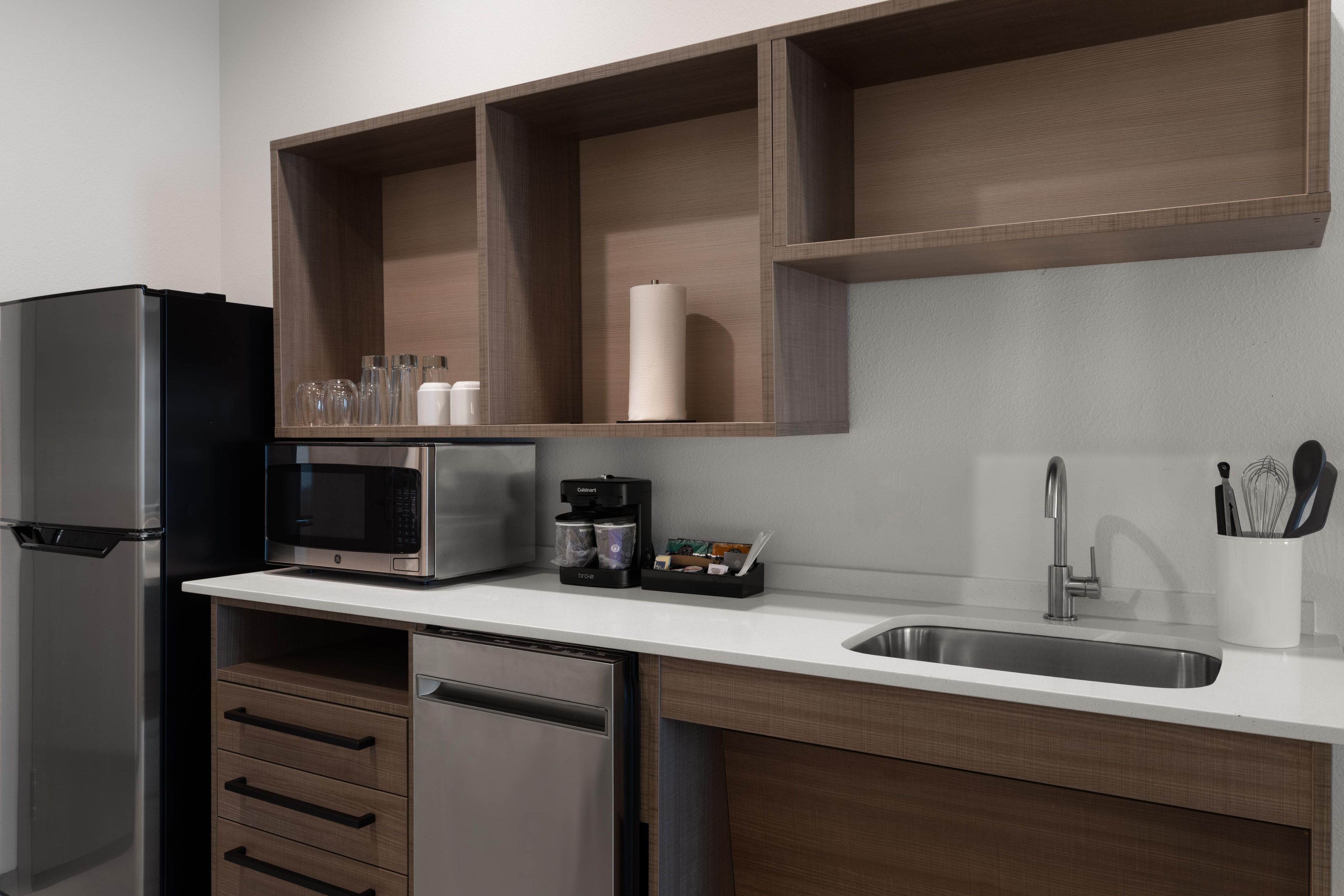 A modern kitchen with a stainless steel refrigerator, a built-in microwave, a coffee maker, and a sink with utensils.