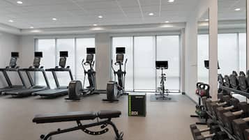 Un gimnasio con cintas de correr, elípticas, una banca y estantes para pesas.