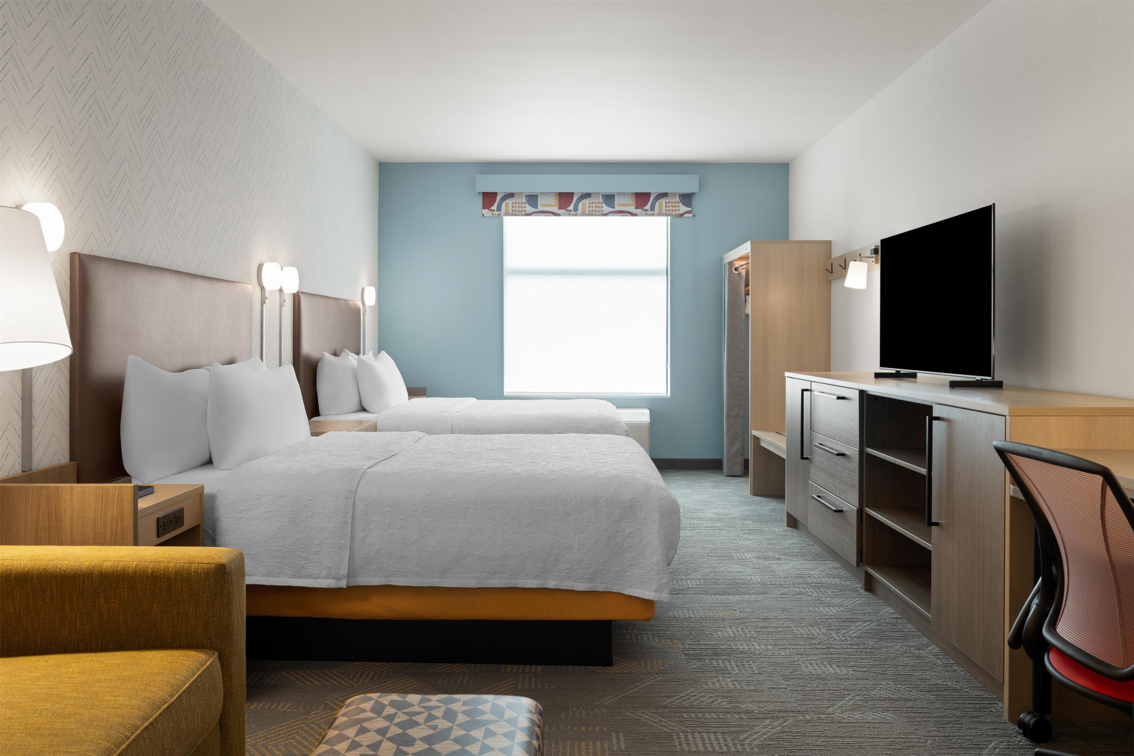 A hotel room with two beds, a desk with a television, a chair, and a wardrobe.
