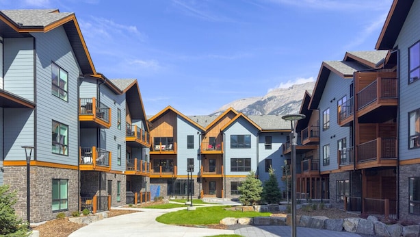 Un immeuble résidentiel moderne à plusieurs étages, doté de balcons, d’une cour intérieure et offrant une vue sur les montagnes.