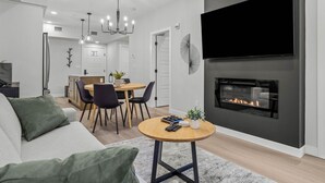Un salon moderne avec une cheminée, un coin repas et une cuisine en arrière-plan.