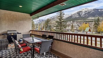 A balcony with a view of mountains, a grill, and outdoor furniture.