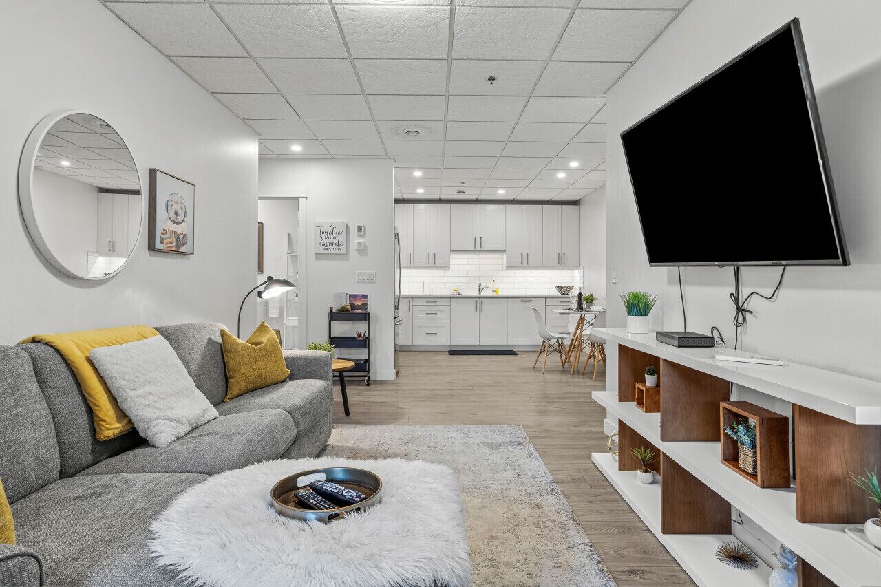 A modern living room with a grey sofa, a round mirror, and a flat-screen TV mounted on the wall.