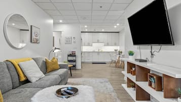A modern living room with a grey sofa, a round mirror, and a flat-screen TV mounted on the wall.