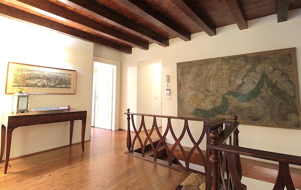 A spacious room with wooden flooring, a staircase with a decorative railing, a desk with a lamp, and a large map on the wall.