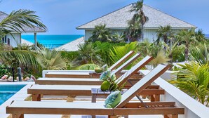 A poolside area with lounge chairs and a view of the ocean. - New Luxury Beachfront Bungalows w/Heated Pool, Pink-Sand Beach (Governors Harbour)