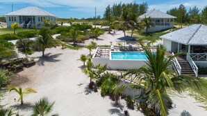 A beachfront property with a swimming pool, multiple beach houses, and lush tropical vegetation. - New Luxury Beachfront Bungalows w/Heated Pool, Pink-Sand Beach (Governors Harbour)