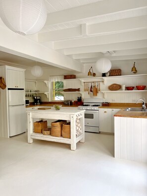 A kitchen with white cabinetry, a central island, and hanging utensils. - Sea Song on Juicy Hill, Short Walk to Pink Sands Beach (Dunmore Town)