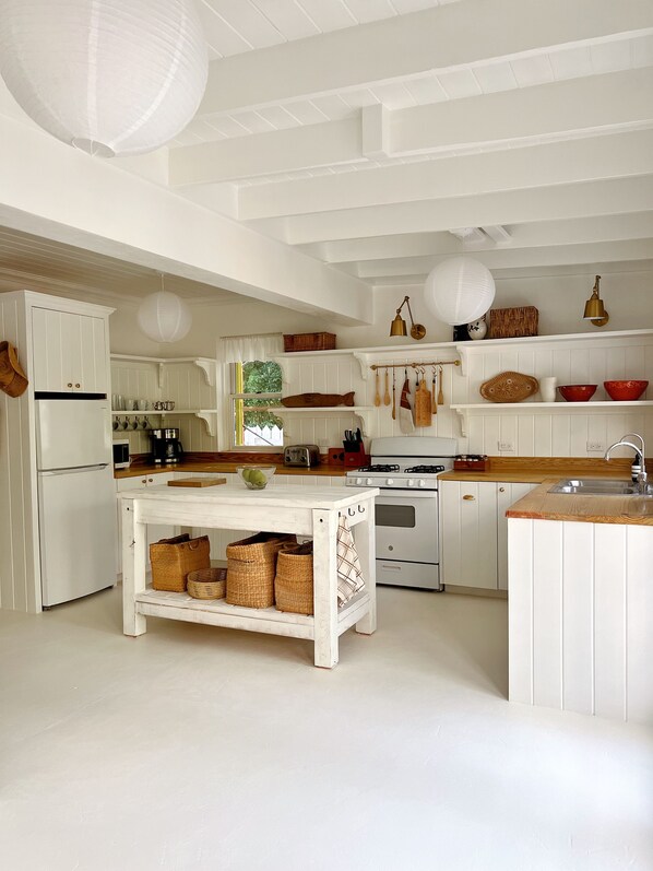 A kitchen with white cabinetry, a central island, and hanging utensils. - Sea Song on Juicy Hill, Short Walk to Pink Sands Beach (Dunmore Town)