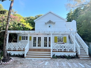 A two-story white house with a covered porch and a staircase leading to the upper level. - Sea Song on Juicy Hill, Short Walk to Pink Sands Beach (Dunmore Town)