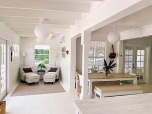 A room with a white color scheme, featuring a dining table, two chairs, a bench, and a potted plant. - Sea Song on Juicy Hill, Short Walk to Pink Sands Beach (Dunmore Town)