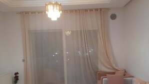 A living room with a white coffee table, a grey rug, a sofa with pink cushions, and a chandelier. - Pool-view apartment in a charming, well-secured residence (Monastir)