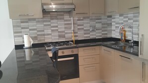 A modern kitchen with a gas stove, a stainless steel range hood, beige cabinets, a black countertop, and a tiled backsplash. - Pool-view apartment in a charming, well-secured residence (Monastir)