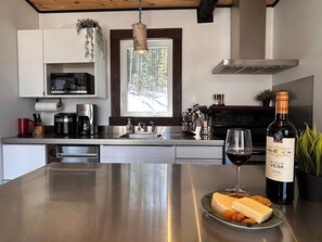 A modern kitchen with stainless steel appliances, a large window, and a wine bottle on the counter.