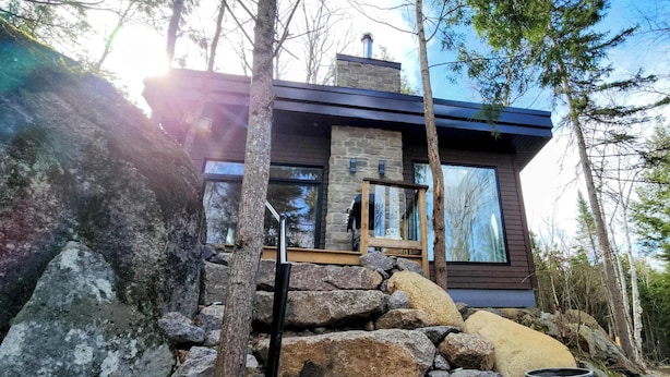 Une cabane moderne avec une façade en pierre, de grandes fenêtres et une terrasse en bois.