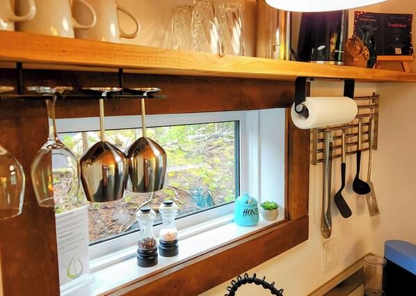 Une cuisine avec des verres à vin suspendus, des salières et des poivrières, une fenêtre donnant sur un beau paysage et des ustensiles de cuisine accrochés au mur.