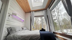 Une chambre avec un puits de lumière, un lit avec des oreillers, une couverture et une fenêtre avec des rideaux.