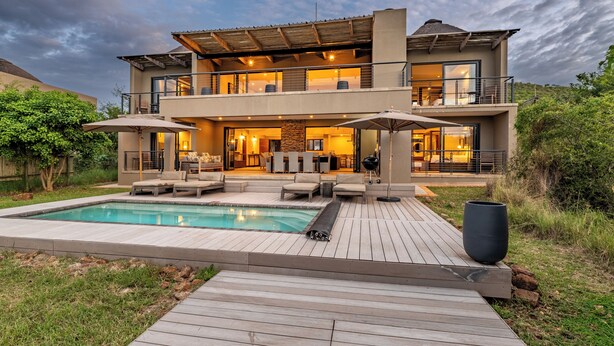 Una moderna casa a due piani con piscina, area salotto esterna e patio.