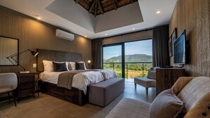 Camera da letto moderna con un letto grande, una scrivania, una sedia, una televisione e un balcone con vista sulle colline.