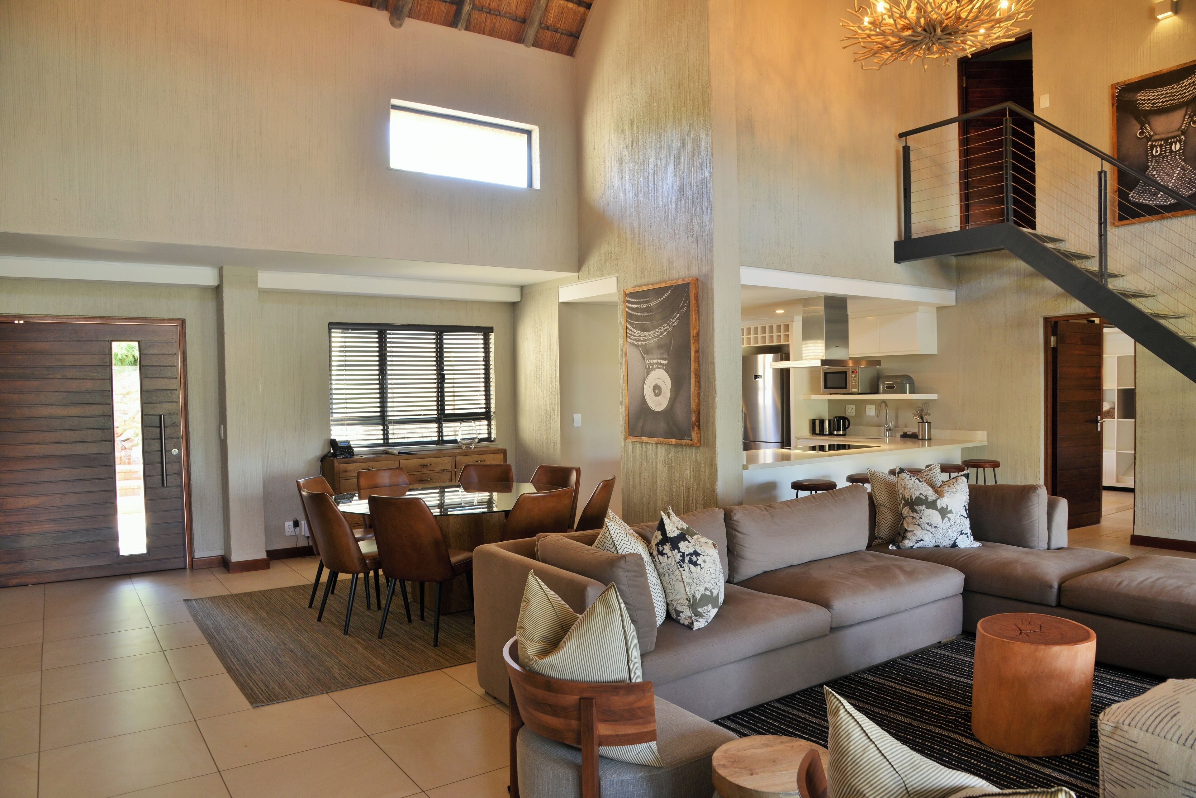 A spacious living area with a large sofa, a dining table, and a staircase leading to an upper level.