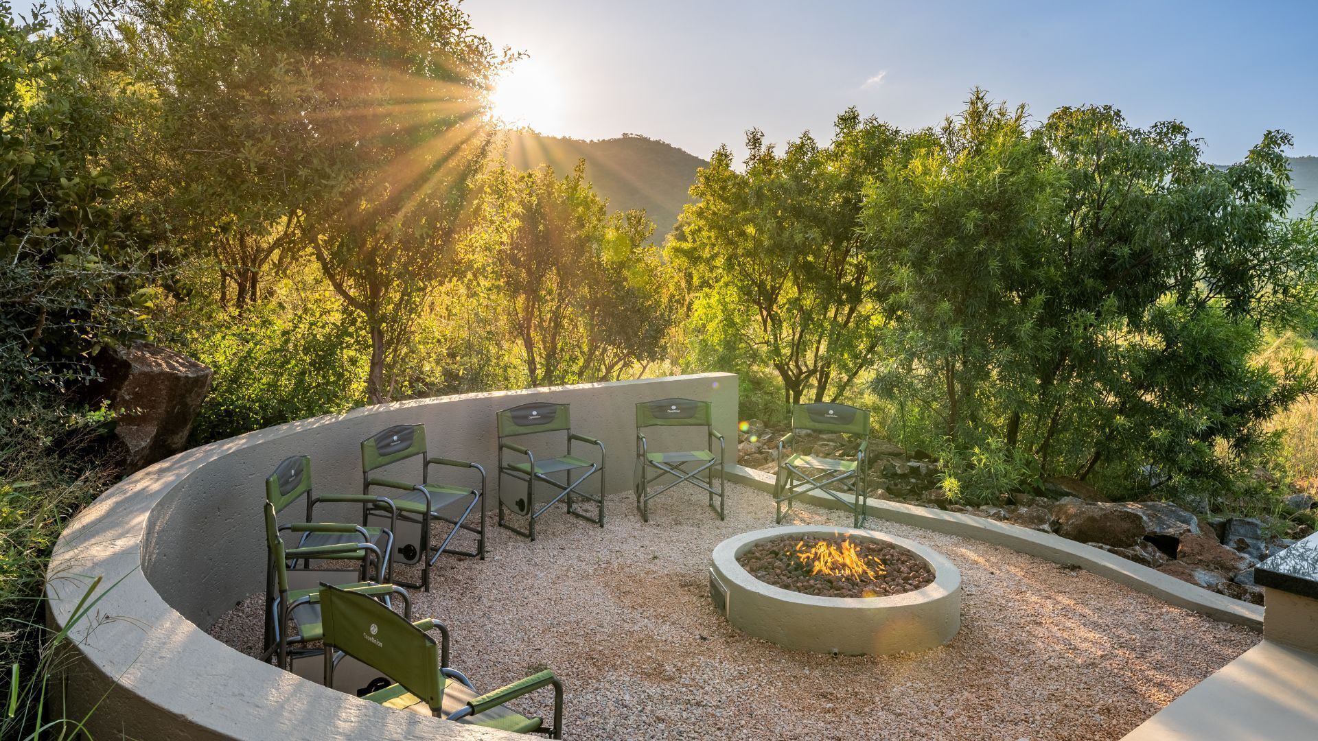A circular outdoor seating area with six chairs and a central fire pit surrounded by gravel.