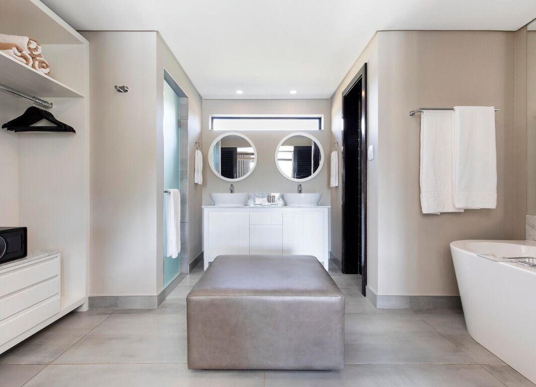 Een moderne badkamer met een grote spiegel, twee wasbakken, een bad en een bankje.